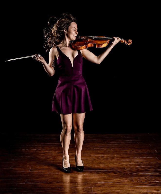 Brianna in a plum dress, playing viola with her hair in motion against a dark background