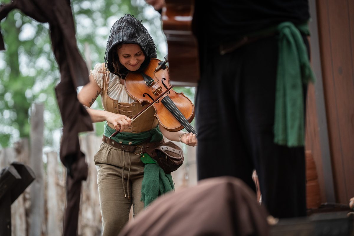 Brianna in Renaissance faire costume, smiling as she plays viola outdoors